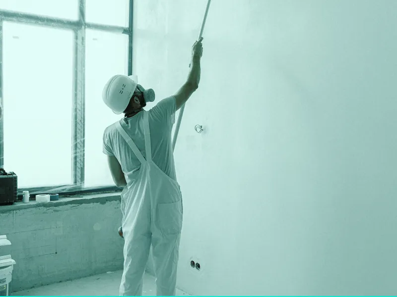 House painter in white overalls rolling paint onto an interior wall