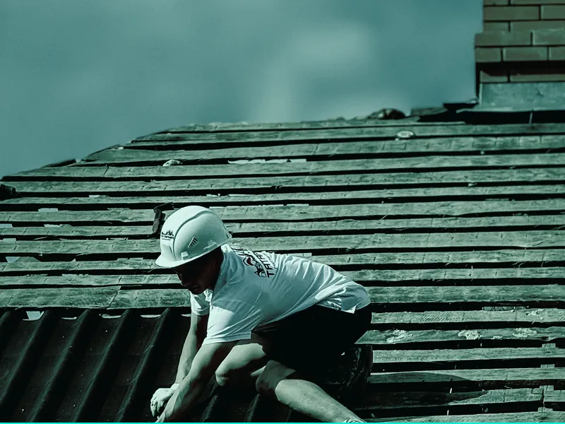 Roofer in safety gear laying roof tiles on a pitched roof